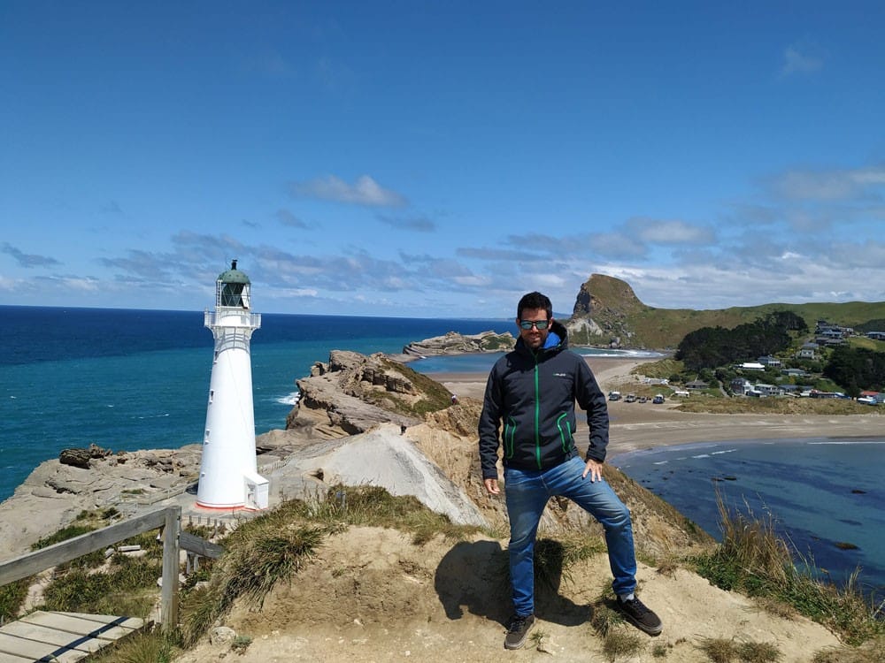 Experiencia Rafa chico moreno con un anorak y unos tejanos posando para cámara y detrás un faro y el cielo despejado
